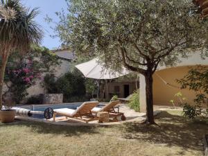 un patio con 2 sillas y una sombrilla junto a la piscina en La Maison Des Autres, piscine chauffée, chambres d'hôtes proches Uzès, Nîmes, Pont du Gard en Saint-Géniès-de-Malgoirès