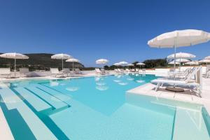 a large swimming pool with white chairs and umbrellas at Capo Falcone Charming Apartments in Stintino