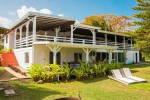 une maison blanche avec une terrasse couverte et quelques plantes dans l'établissement Villa Cristalline Douceur des Alizés, à Belle-Allée