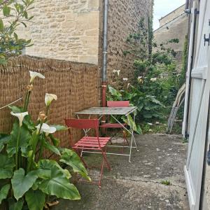 two red chairs and a table in a garden at Maison au cœur du bourg de Creully - 8km de la mer in Creully