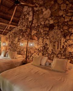 - une chambre avec 2 lits et un mur en pierre dans l'établissement Kapok Bacalar - Plant Based Hotel, à Buenavista