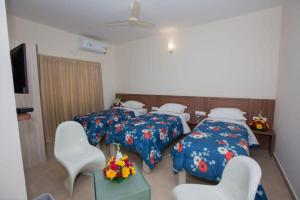 Zimmer mit 3 Betten und 2 Stühlen sowie einem TV in der Unterkunft HOTEL VIJAYA LAKSHMI RESIDENCY - YESHWANTHPUR in Bangalore