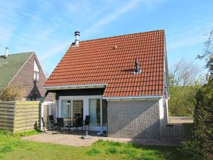 uma pequena casa com telhado vermelho e cadeiras em Ferienhaus HET GANZELAND OOST100 em Oostmahorn