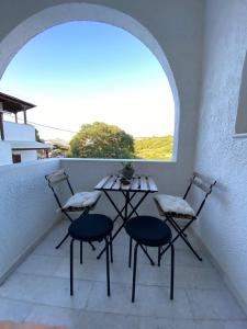 una mesa y sillas en un balcón con ventana en On the road house en Apérathos