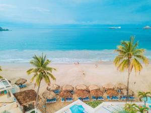 einen Strand mit Sonnenschirmen, Palmen und dem Meer in der Unterkunft Fontan Ixtapa in Ixtapa