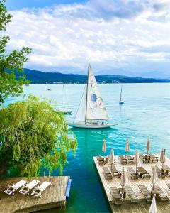 a sail boat on a lake with chairs and a dock at Hotel Schloss Leonstain in Pörtschach am Wörthersee