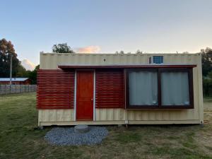 una casita con una puerta roja en un campo en Cabañas Habitainer 2, en Pucón