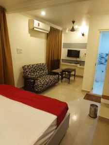 a bedroom with a bed and a chair and a television at Hotel Menaka in Vijayawāda