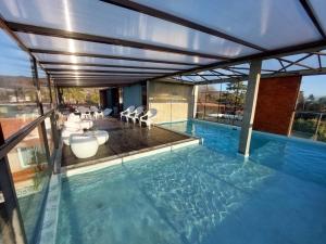 uma piscina com cadeiras brancas e uma grande parede de vidro em Costalago Suites- By HVH em Villa Carlos Paz