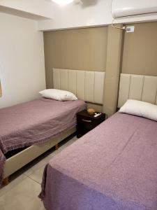 two beds in a bedroom with purple sheets and a table at Ganesha Abasto Apartments in San Miguel de Tucumán