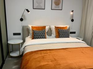 a bedroom with a bed with an orange blanket and pillows at Alėjos Apartmentai City in Druskininkai