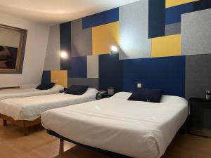 three beds in a room with a colorful wall at Brit Hotel Dijon Centre Gare in Dijon