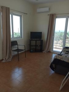 sala de estar con TV, silla y ventanas en Nereids Apartments-Agavi, en Petalidi
