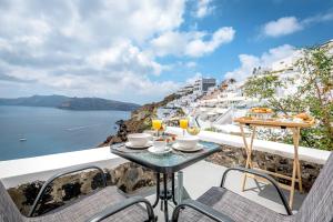 una mesa y sillas en un balcón con vistas al océano en Amazing View Villa Oia with Jacuzzi en Oia