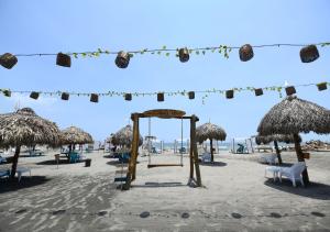 een strand met rieten parasols en stoelen en een schommel bij Imagine Beach in Puerto Colombia