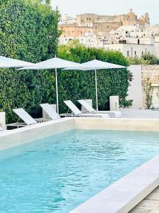 una piscina con sedie bianche e ombrelloni di Casa d'Autore a Ostuni