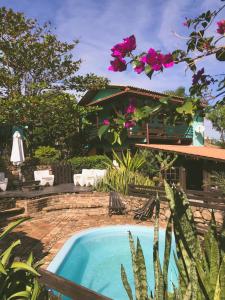 una piscina frente a una casa con flores rosas en Haleakala Hostel & Pousada en Praia do Rosa