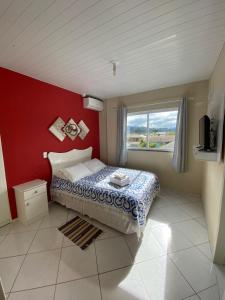 1 dormitorio con 1 cama con pared roja y ventana en Pousada Arcanjo Rafael, en Urubici