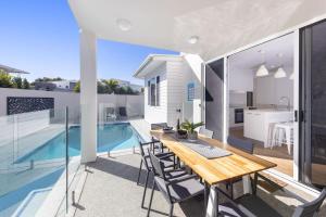 a dining table on the balcony of a house with a swimming pool at Waves Beach House in Marcoola