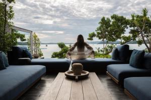 a woman sitting on a couch looking out at the water at Clay Beach Samui in Nathon Bay