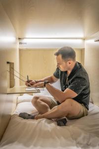 a man sitting on a bed looking at his cell phone at Panda Pod Hotel in Richmond +37 photos