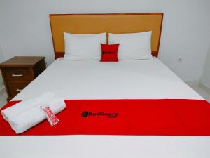 a white bed with a red blanket and towels on it at RedDoorz at Omah Candi Sari near Airport YIA in Yogyakarta