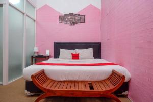 RedDoorz At Golden Inn Tugu Yogyakarta في يوغياكارتا: غرفة نوم ذات جدران وردية مع سرير مع مقعد
