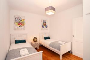two beds in a room with white walls and wood floors at Happy Holiday Cascais - Garden in Cascais