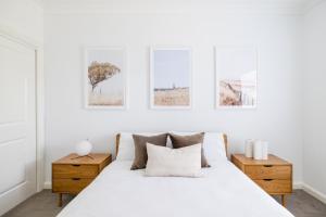 a white bedroom with a white bed and some pictures on the wall at Kuzman Estates in Mudgee