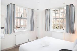 a white bedroom with two windows and a bed at Goodenough College – University Residence in London