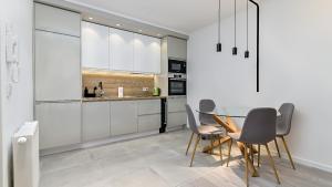 Apartman Nostra 1 في زغرب: مطبخ مع دواليب بيضاء وطاولة زجاجية وكراسي