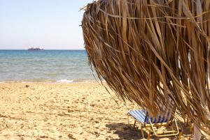 uma cadeira debaixo de um guarda-sol de palha numa praia em Ionio Holidays Katerina Apartments em Vasilikos