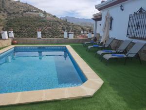 a swimming pool on a lawn with chairs around it at Casa rural Villa Miradri in Torrox