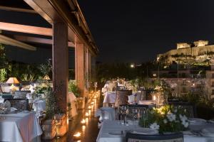 - un restaurant avec des tables et des chaises blanches la nuit dans l'établissement Royal Olympic Hotel, à Athènes