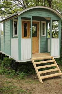 a green and white tiny house with a porch at The Kestrel Shepherd Hut, Whitehouse Farm in Stowmarket