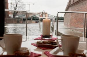 a candle in a vase on a table with two cups at Apartament na wodzie - Riveraparts - Marina Oława in Oława