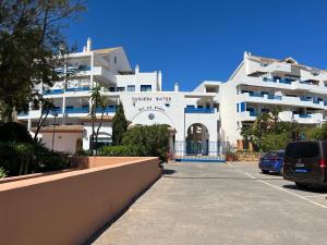 a large white building with cars parked in a parking lot at Puerto de la Duquesa MINIMUM 3 NUITS in Manilva