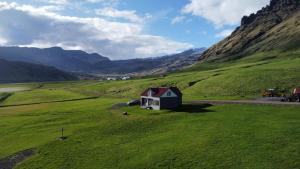 a small white house in a green field with mountains at Guesthouse Rauðafell in Holt