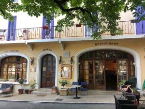 a woman sitting in a chair in front of a building at Logis Hôtel Restaurant Le Louvre in Sault-de-Vaucluse