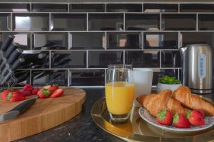 un tavolo con un bicchiere di succo d'arancia, croissant e fragole di K Suites - Palmer Park - 4 Bedroom a Reading