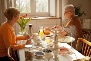 dos personas mayores sentadas en una mesa comiendo comida en B&B De Kersentuin, en Borgloon