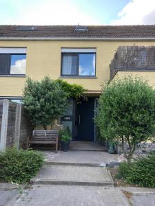 uma casa amarela com uma porta azul e duas árvores em La MER em Bredene
