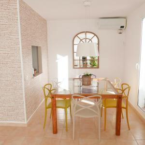 a dining room with a glass table and yellow chairs at Es Cucó in Cala Galdana