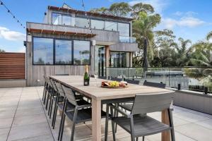 a dining table and chairs on a patio with a house at Beachfront Escape - 6 bedroom, Pool & beach access in Merimbula