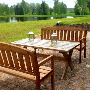 drewniany stół piknikowy z 2 ławkami i jeziorem w obiekcie Villa Murmuļmuiža w mieście Zāģeri