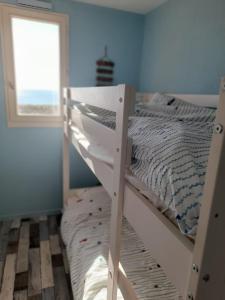 białe łóżko piętrowe w niebieskim pokoju z oknem w obiekcie T3 avec magnifique vue mer w mieście Le Barcarès