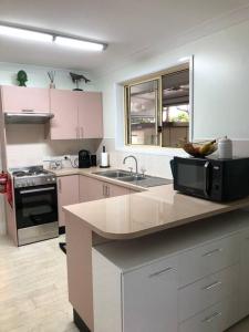una cucina con armadi rosa, lavandino e forno a microonde di Pet friendly home with pool and boat parking. a Iluka