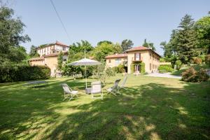 eine Liegewiese mit Stühlen und einem Regenschirm vor einem Haus in der Unterkunft Bright APT surrounded by greenery with parking & Shared Pool in Villa Guardia