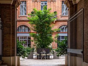 a tree in front of a building with tables and chairs at Ibis Styles Toulouse Capitole in Toulouse