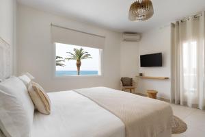 a white bedroom with a palm treeseen from a window at Finikas Hotel in Aliko Beach